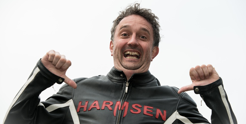 Marcel Harmsen grinning, holding open a black racing jacket with HARMSEN across it