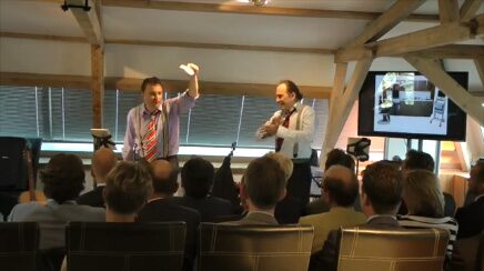 Two performers working a seated conference audience in a timber-framed hall